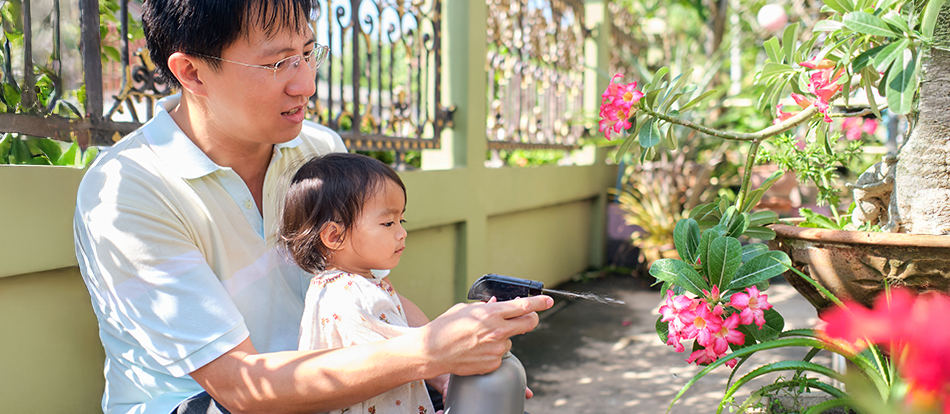 young child helps her father water plants in the garden
